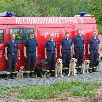 Die Mitglieder stehen gemeinsam mit ihren Hunden vor dem Wagen der Rettungshundeeinheit.
