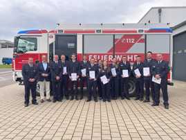 Gruppenfoto: Eine Reihe von Feuerwehrfrauen und Feuerwehrmännern halten ihre Urkunden in der Hand. Sie stehen vor einem Feuerwehrauto.
