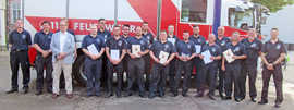 Die geehrten Mitglieder der Freiwilligen Feuerwehr Ehrang stehen vor einem Feuerwehrfahrzeug und halten ihre Urkunden in den Händen.