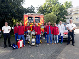 Das ECMO-Team des Brüderkrankenhauses Trier steht gemeinsam mit Thomas Reinholz, dem Leiter des Rettungsdienstes der Feuerwehr (ganz rechts) und Ralf Cordel von der Berufsfeuerwehr (ganz links) vor dem Intensivtransportwagen und dem Begleitfahrzeug. Sie zeigen die Herz-Lungen-Maschine.