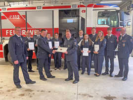 Feuerwehrmänner und- frauen stehen in Uniform mikt Urkunden vor einem Löschfahrzeug.