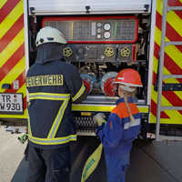 Ein Feuerwehrmann und ein Mitglied der Jugendfeuerwehr schließen gemeinsam einen Schlauch an.