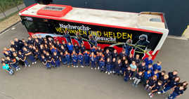 Rund 70 Kinder und Jugendliche der Jugendfeuerwehr Trier stehen im Halbkreis vor einem Bus. Auf dem Bus steht: Nachwuchs-Heldinnen und Helden gesucht.