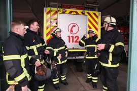 Fünf Feuerwehrmänner stehen in der Fahrzeughalle vor einem Feuerwehrfahrzeug und unterhalten sich.