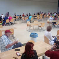 Menschen sitzen und unterhalten sich in einem großen Saal, dere mit Tischen und Stühlen ausgestattet ist.