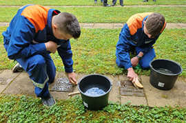 Zwei junge Feuerwehrmänner reinigen Grabplatten sowjetischer Kriegsopfer.