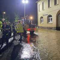 Feuerwehrleute in blau-gelber Einsatzkleidung besprechen sich am Rand der Überschwemmungszone.