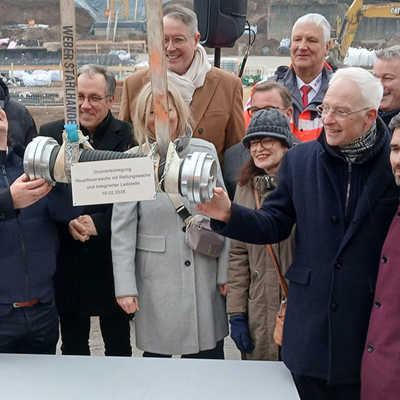 Die von den Projektbeteiligten befüllte Zeitkapsel hängt an einem Kran, der sie an die vorgesehene Stelle in der Baugrube befördert.