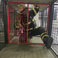 Ein Atemschutzgeräteträger klettert mit seiner Ausrüstung durch die enge Atemschutzübungsstrecke.