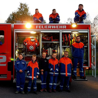 Neun Kinder stehen in Feuerwehrkleidung vor einem Feuerwehrauto.