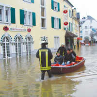 Ein Boot mit drei Personen wird von zwei Feuerwehrleuten durch das Hochwasser gezogen.