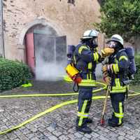 Zwei Feuerwehrmänner stehen vor einem Gebäude aus dem Rauch kommt und überprüfen ihre Atemschutzmasken.