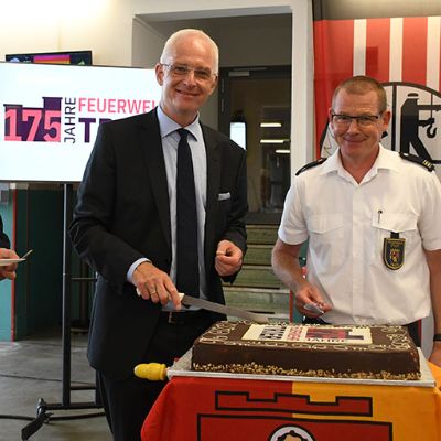Feuerwehrchef Andreas Kirchartz und OB Wolfram Leibe schneiden gemeinsam mit Stadtfeuerwehrobmann Johannes Haag (v. r.) als Vertreter der Freiwilligen Feuerwehren den Kuchen an.